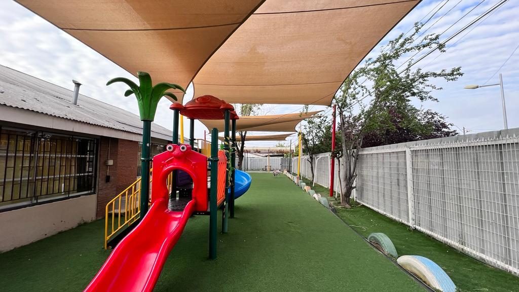 Velas de sombra sobre el patio de juegos de un jardín infantil con juegos plásticos y pasto sintético