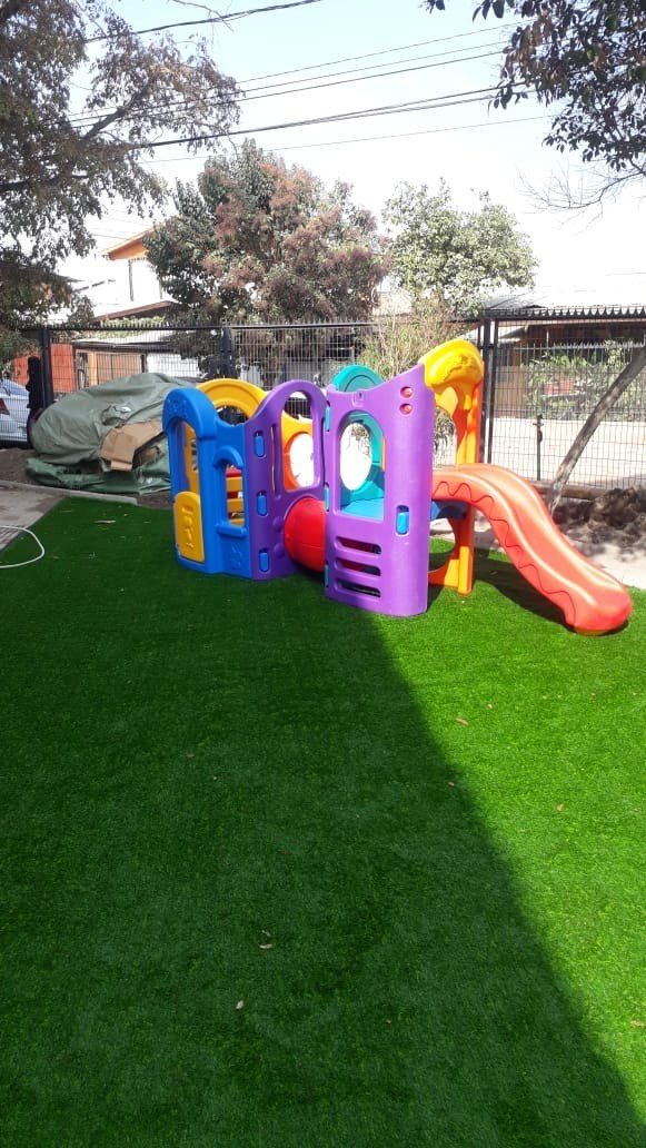 Juego infantil sobre pasto sintético en el patio de un establecimiento educacional