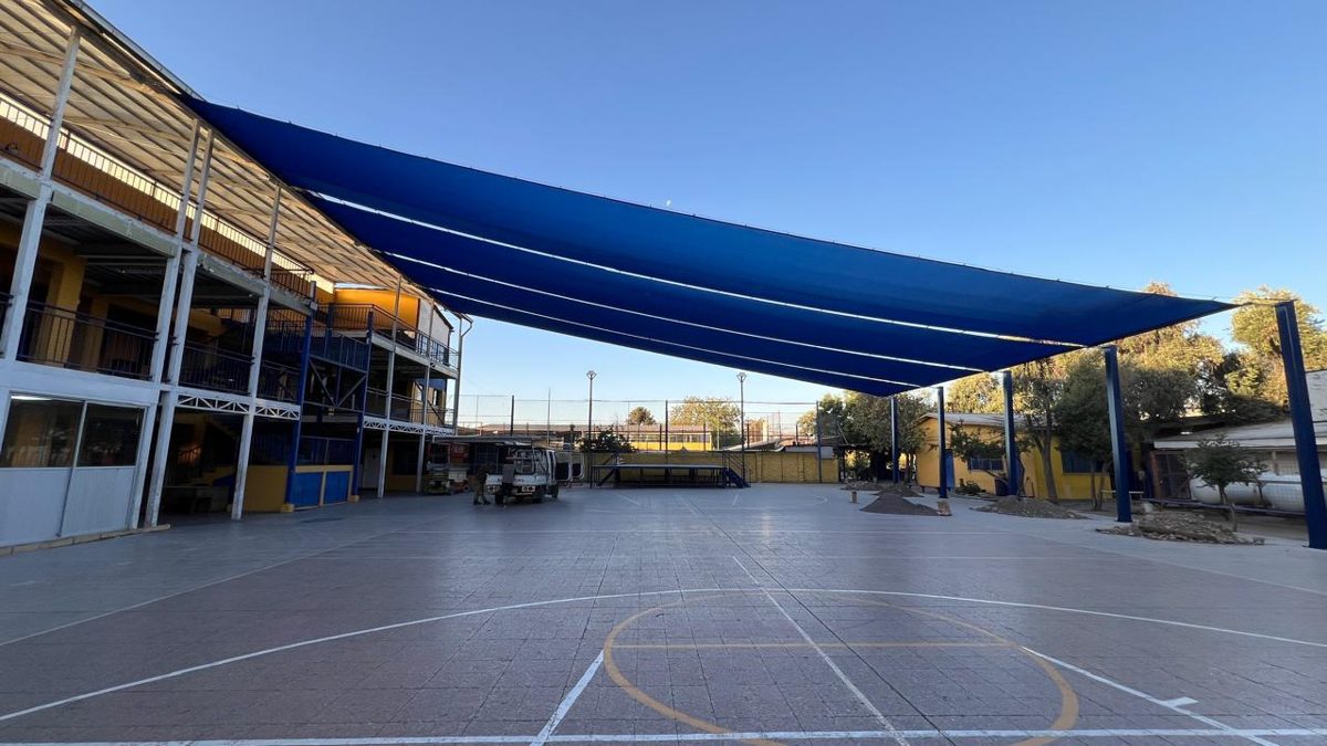 Gran vela de sombra azul tensada sobre la multicancha de un establecimiento educacional