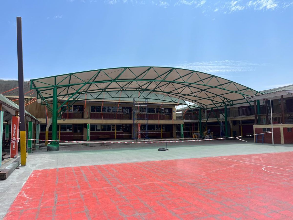 Montaje del velario en arco con andamios y cinta de seguridad durante la instalación en el patio del colegio
