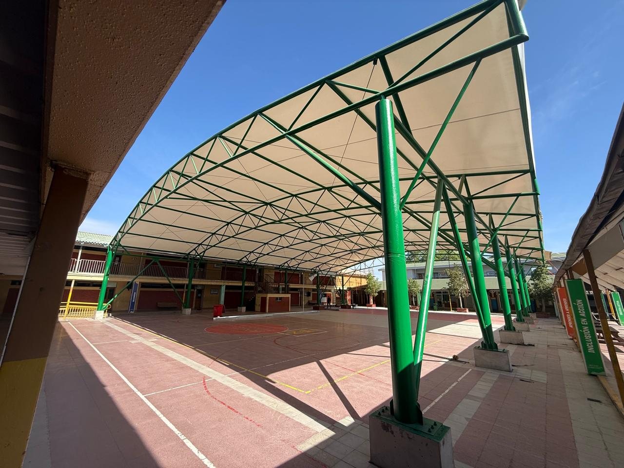 Velario terminado con estructura metálica verde en arco y membrana tensada sobre la multicancha de un colegio
