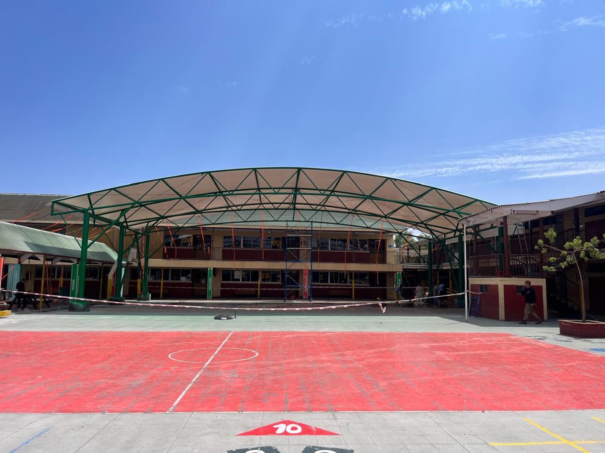 Velario con estructura metálica en arco de color verde sobre el patio central de un colegio